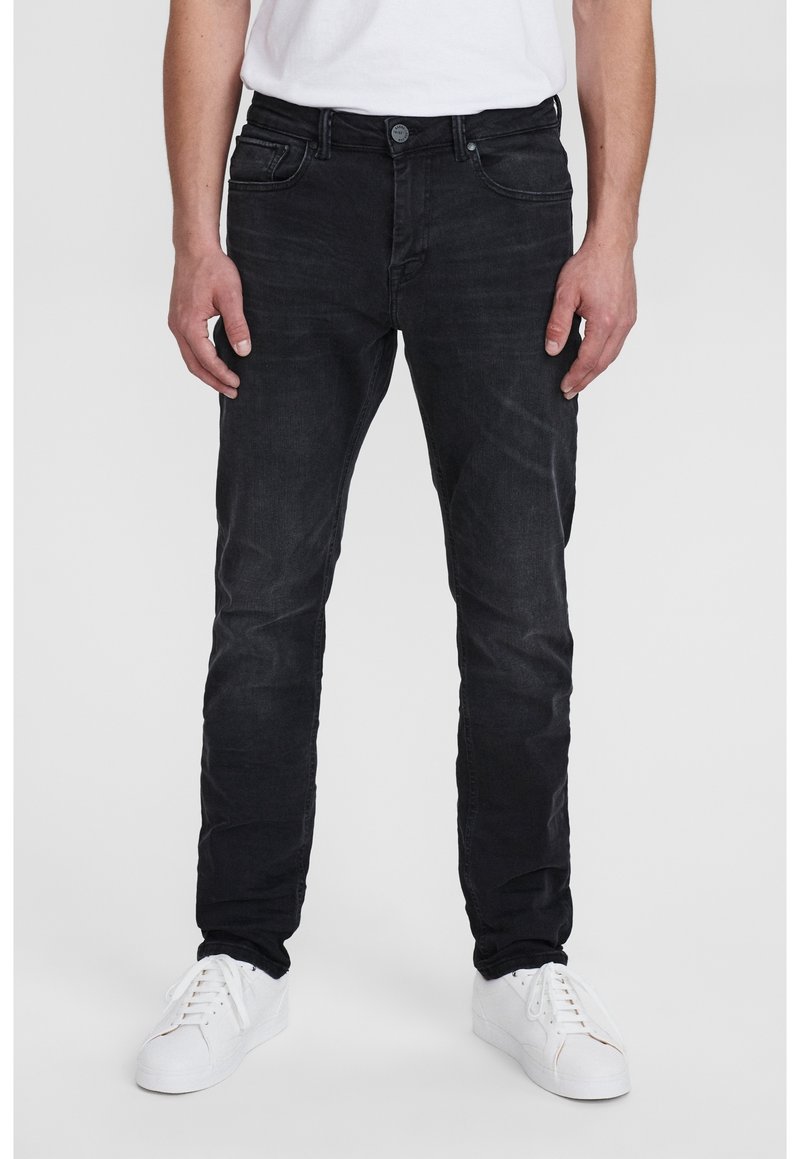 Černé slim-fit džíny vyrobené z denimu, s předními kapsami, zapínáním na knoflík a mírným vyblednutím. Doplňují je bílé tenisky.