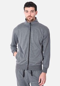 Giacca da track grigia con zip, colletto alto, maniche lunghe e polsini a coste; presenta una zip nera e pantaloni grigi abbinati con fettuccia.