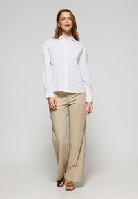Camicia bianca con bottone, maniche lunghe, abbinata a pantaloni beige a gamba larga. La camicia presenta un colletto classico e una vestibilità comoda.