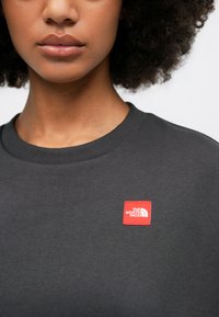 Γκρίζα φανέλα 100% βαμβακερή με στρογγυλή λαιμόκοψη και μια μικρή κόκκινη ετικέτα στο αριστερό πλευρό, που αναγράφει "THE NORTH FACE."