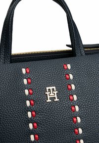Borsa in pelle di colore blu navy con una finitura testurizzata, caratterizzata da dettagli di cucitura rossa e bianca e un logo dorato sulla parte anteriore.