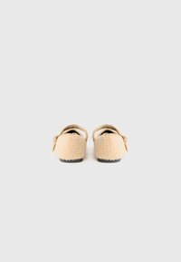 Beige, fluffiga tofflor med rem och spänne, sedda bakifrån mot en helt vit bakgrund.