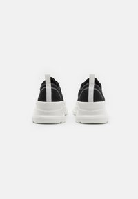 Schwarze Stoff-Sneaker mit weißen Gummisohlen, mit einem Zugband an der Ferse und kontrastierenden Nähdetails.