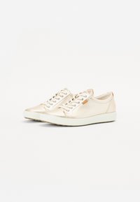 Paire de baskets basses crème à lacets, semelles blanches, dessus en cuir lisse et étiquette de marque marron sur le côté.
