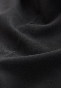 Tissu noir doux avec des plis subtils et une texture lisse, montrant un tissage détaillé et un drapé délicat.