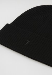 Černá pletená čepice s žebrovanou strukturou a ohrnutým lemem, s jemně vyraženým černým logem na přední straně.
