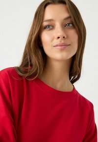 Sudadera de algodón roja con cuello redondo y mangas largas, que presenta una textura suave y un ajuste holgado.