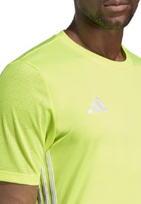 Felgeel sportshirt met een gladde textuur en meshpanelen, voorzien van het witte Adidas-logo en drie witte strepen aan de zijkant.