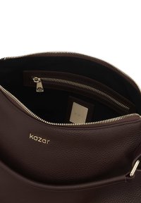 Brązowa torebka skórzana o teksturowanej powierzchni z złotym suwakiem, wyposażona w wykładzinę z tkaniny wewnątrz oraz małą kieszonkę na zamek. Wewnątrz wytłoczone logo.