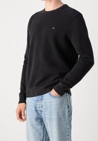 Schwarzer, gerippter Sweatshirt mit Rundhalsausschnitt, ausgestattet mit einem kleinen Logo auf der Brust, kombiniert mit hellblauen Jeans.