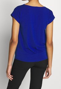 Top corto de manga corta azul hecho de una tela suave, con un escote redondo y un corte relajado, con un sutil detalle de costura en el centro de la parte posterior.