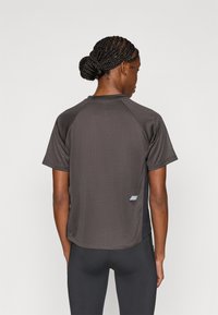 Γκρι αθλητική μπλούζα με υφασμάτινη υφή, κοντά μανίκια και ελαφρώς χαμηλωμένο στρίφωμα, με μαύρο πλαϊνό πάνελ και αντανακλαστική λεπτομέρεια.