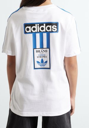 Osoba nosząca białą koszulkę Adidas z niebieskim logo z trzema paskami i napisem „The brand with the three stripes” na plecach.