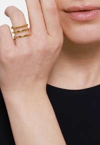 Anelli d'oro impilati sulle dita, con superfici lisce e larghezze variabili. Un design semplice con un anello decorato con piccole perline.