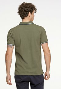 Oliven grøn polo t-shirt med krave, korte ærmer og marineblå detaljer på kraven og ærmerne. Tekstureret stof, tætsiddende design.