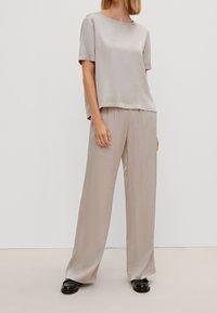 Top in satin beige chiaro con maniche corte e scollatura rotonda, abbinato a pantaloni larghi coordinati. Entrambi i capi hanno una texture liscia.