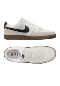 Zapatillas de cuero blanco con un logo de Nike Swoosh en negro, que cuentan con una mediasuela beige y una puntera perforada para mayor transpirabilidad. Incluyen una suela texturizada.