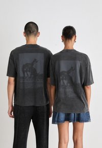 Black oversized t-shirts made of soft fabric, featuring rear graphic designs of a camel. Short sleeves and a relaxed fit.