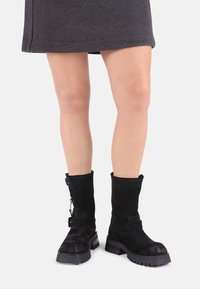 Cizme negre din suede, până la jumătatea pulpei, cu un finisaj texturat, având un fermoar lateral, detalii cu curea și tălpi din cauciuc groase.