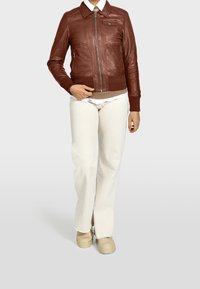 Brun läderjacka med dragkedja, krage och framfickor; kombinerad med ljusfärgade vida byxor och beige skor.