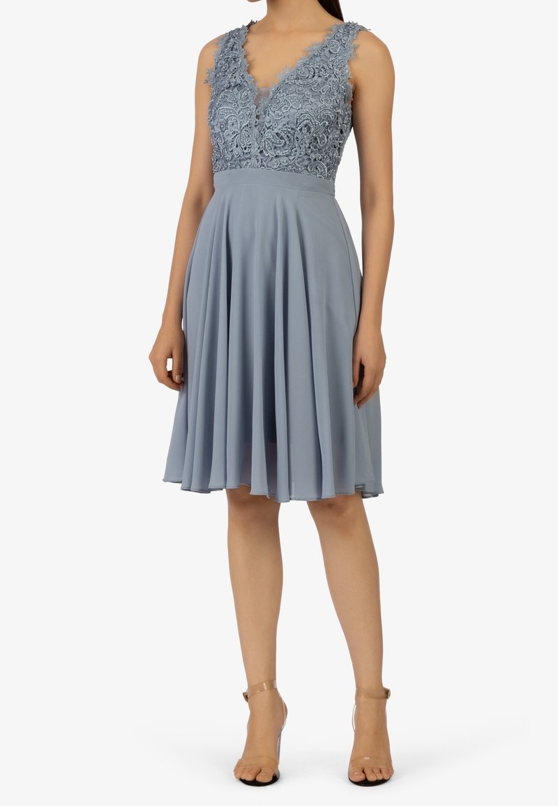 Robe bleu clair avec un col en V et un corsage en dentelle, présentant une jupe plissée. Le tissu semble doux, avec une texture fluide et une broderie détaillée.