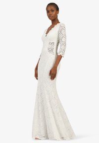 Spitzenkleid mit Dreiviertelärmeln, gewelltem Halsauschnitt, tailliertem Oberteil, ausgestelltem Rock und zwei Taschen vorne. Farbe: weiß.
