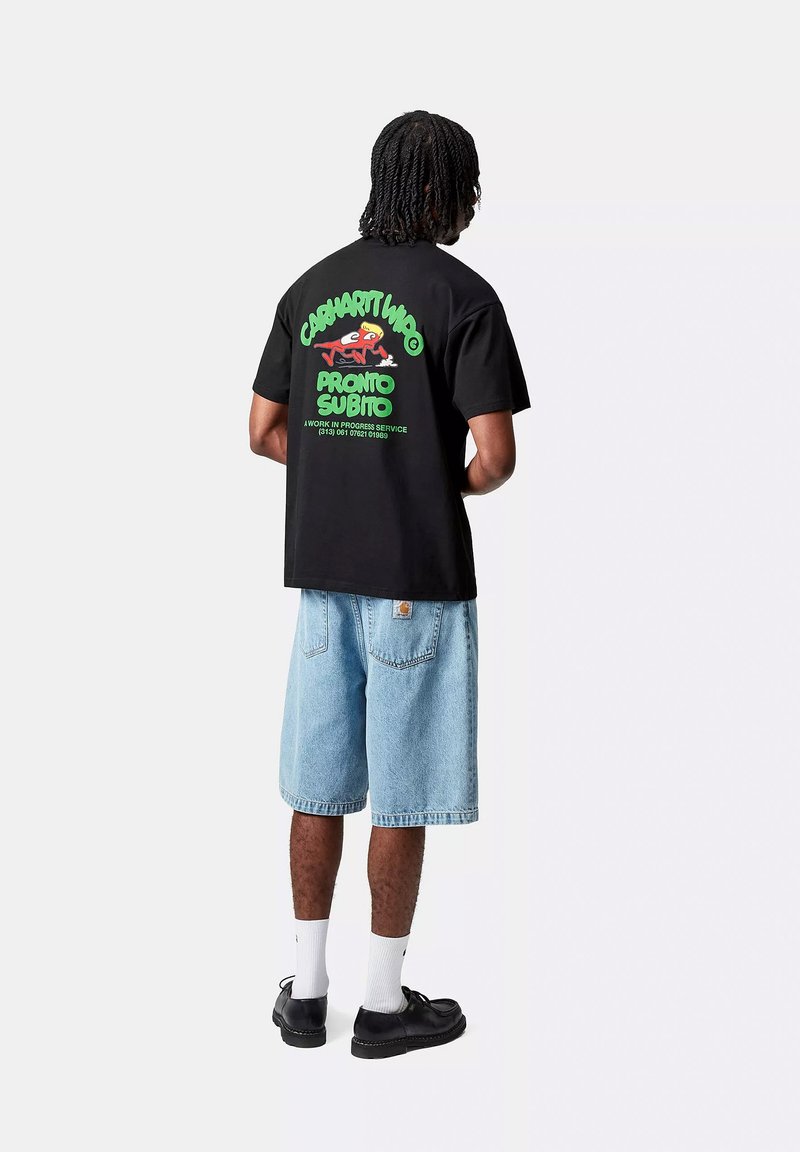 Black cotton t-shirt featuring bold green and red graphic text on the back, paired with light blue denim shorts and black shoes.