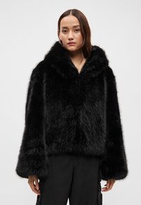 Juodas dirbtinės kailio paltas su plačia apykakle, laisvo silueto ir ilgomis rankovėmis. Turi minkštą, tekstūruotą paviršių ir minimalistinę aparatūrą.