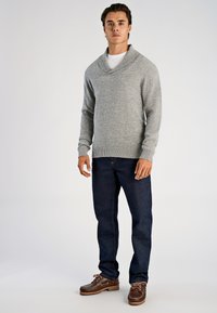 Gråstickad tröja med djup sjalkrage, kombinerad med mörkblå jeans och bruna båtskor. Mjuk textur och casual design.