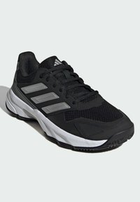 Zapatilla deportiva negra con parte superior de malla, tres rayas grises, suela acolchada y suela de goma. Incluye cordones y un collar acolchado para mayor comodidad.