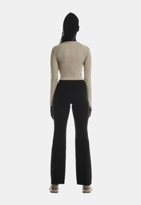Haut beige à manches longues avec une coupe ajustée, associé à un pantalon noir évasé. La tenue présente une silhouette élégante et une texture lisse.