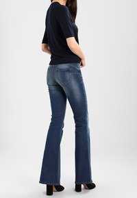 Top navy de manga corta combinado con jeans azules acampanados. Los jeans presentan sutiles detalles de costura y un acabado ligeramente desgastado, complementados con tacones negros.