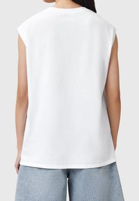 Top de algodón blanco sin mangas con un escote redondeado y costuras de hombro ligeramente caídas. Corte relajado con una textura suave.