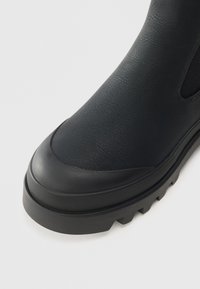 Zwarte enkelboot met een gestructureerde synthetische bovenkant, rubberen neus en een chunky, geribbelde zool. Elastische zijpanelen voor gemakkelijk aan- en uittrekken.