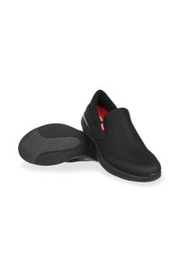 Scarpe nere slip-on con una tomaia in rete traspirante, suola in gomma con grip testurizzato e accenti interni rossi per comfort e supporto.