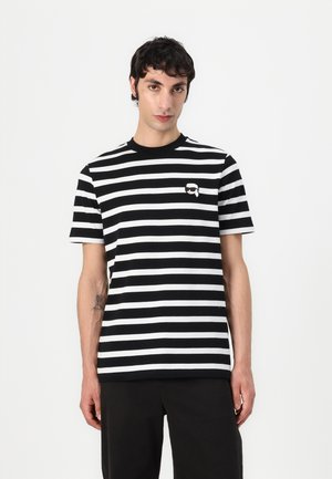 T-shirt rayé noir et blanc, à manches courtes, avec un col rond, ornée d'un petit logo graphique sur la poitrine gauche. Tissu en coton lisse.