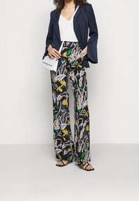 Blommönstrade byxor i svart med gula och gröna accentfärger, kombinerade med en mörk blazer och en vit topp. Har en avslappnad, utsvängd passform.