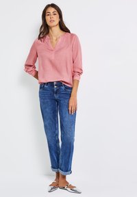Blusa rosa chiaro a maniche lunghe con scollatura a V e polsini arrotolati, abbinata a jeans blue straight-leg e ballerine con punta argentata.