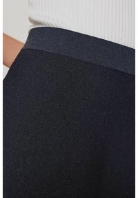 Musta teksturoidu kangas, jossa on poimuttettu vyötärönauha. Materiaali vaikuttaa pehmeältä ja joustavalta, ja siinä on tyylikäs, virtaviivainen muotoilu.