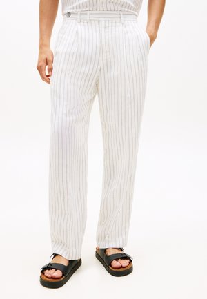 Hvide bukser med tynde lodrette grå striber båret sammen med sorte sandaler med spænde på lys baggrund.
