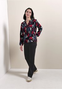 Camicia a maniche lunghe con motivi a zig zag multicolori su sfondo nero; abbinata a pantaloni neri e sneaker bianche.