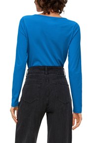 Langärmliges blaues Baumwolloberteil kombiniert mit hoch taillierten schwarzen Denim-Hosen mit hinteren Taschen und einem strukturierten Bund.