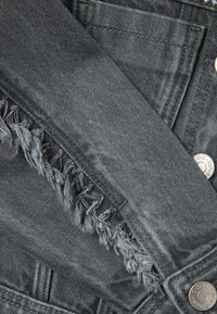 Chaqueta de mezclilla gris con bordes deshilachados en los puños y un botón a presión metálico. Tejido texturizado con un diseño clásico y un ligero desgaste.