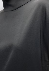 Gros plan d'une personne portant un pull à col roulé gris foncé lisse avec une texture de tissu légèrement brillante.