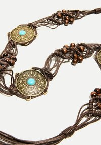 Collana in macramè marrone con accenti circolari in bronzo dai disegni intricati e pietre turchesi, completata da perle di legno.