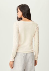 Helles pinkes Longsleeve-Oberteil mit weit geschnittenem Halsausschnitt und schmaler Passform, aus weichem Material hergestellt. Kombiniert mit grauen Jogginghosen, die zwei Gesäßtaschen haben.