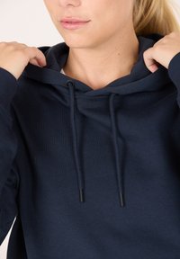 Sudadera azul marino hecha de una tela suave con capucha ajustable, que cuenta con un bolsillo tipo canguro en la parte frontal y puños acanalados para mayor comodidad.