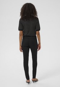 Svart och vit randig kortärmad topp med avslappnad passform, ihop med åtsittande svarta byxor och svarta klacksandaler. Bakvy.