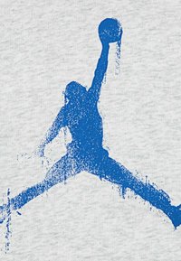 Tessuto grigio con una grande silhouette blu di una figura che salta, in possesso di un pallone da basket, rappresentata con un effetto spray-paint testurizzato.