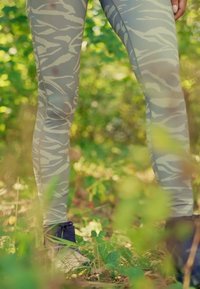 Helle graue Leggings mit einem subtilen weißen Zebra-Streifenmuster; getragen mit dunkelblauen Knöchelstiefeln in einer natürlichen grünen Umgebung.